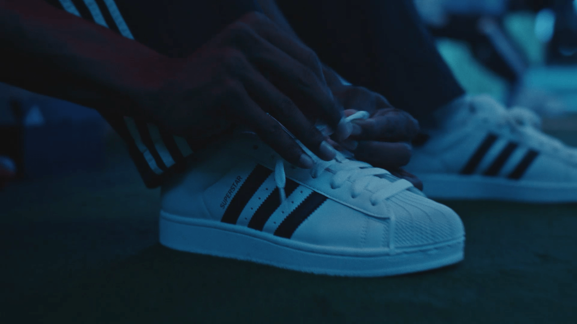 A close up on a pair of adidas shoes with hands tying the laces.