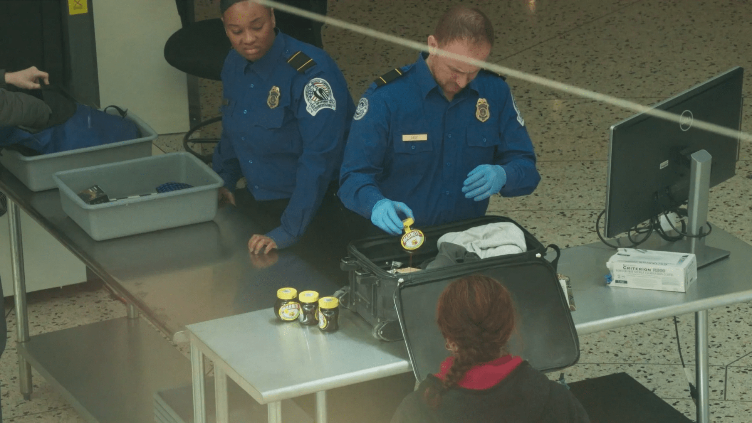 An image of airport security inspecting a suitcase filled with Marmite jars